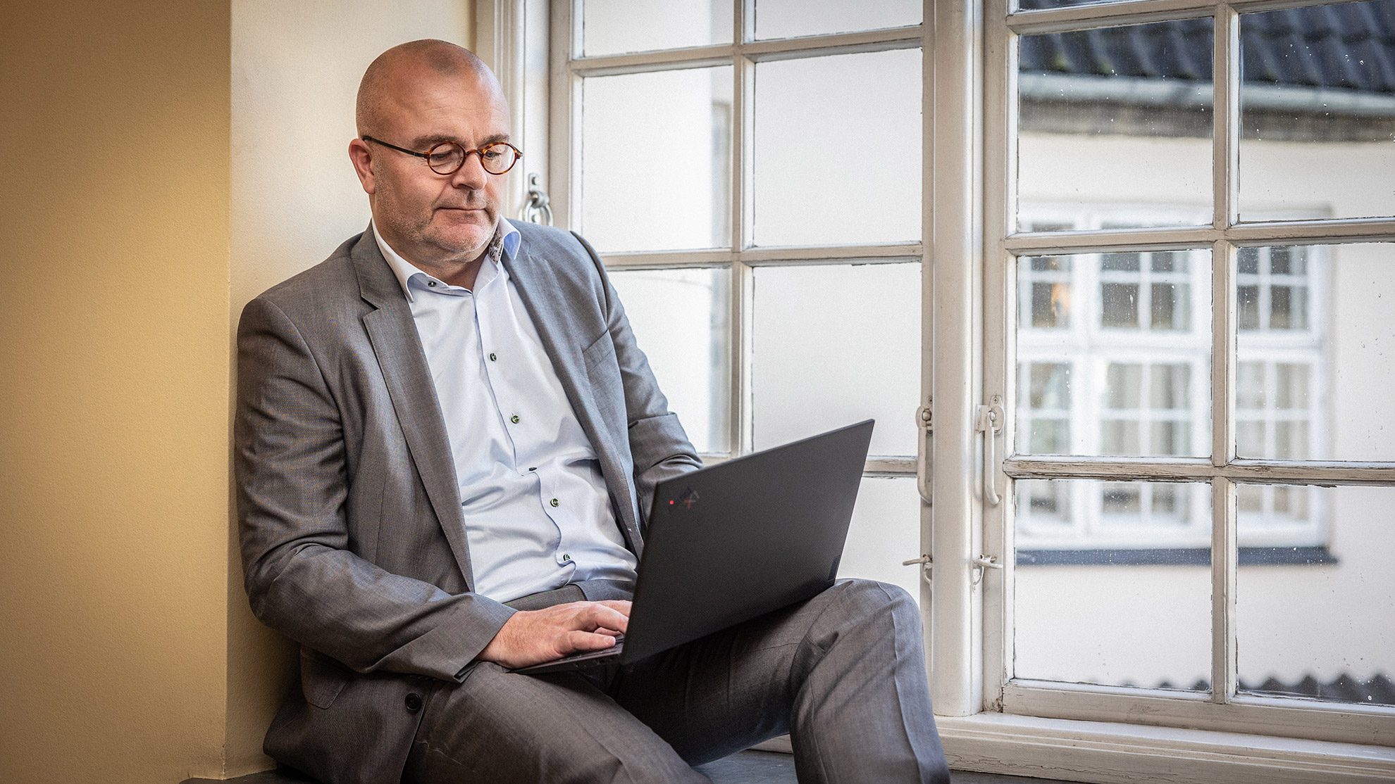 Søren Overbeck, indehaver af Peoplematter, sidder ved et vindue med en bærbar computer.